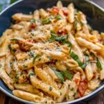 Close-up of Marry Me Chicken Pasta showing creamy texture and golden chicken slices, garnished with fresh basil on a ceramic plate.
