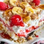 No-Bake Banana Split Cake on a marble countertop, showcasing its creamy layers, fresh fruit, crushed nuts, and whipped topping.