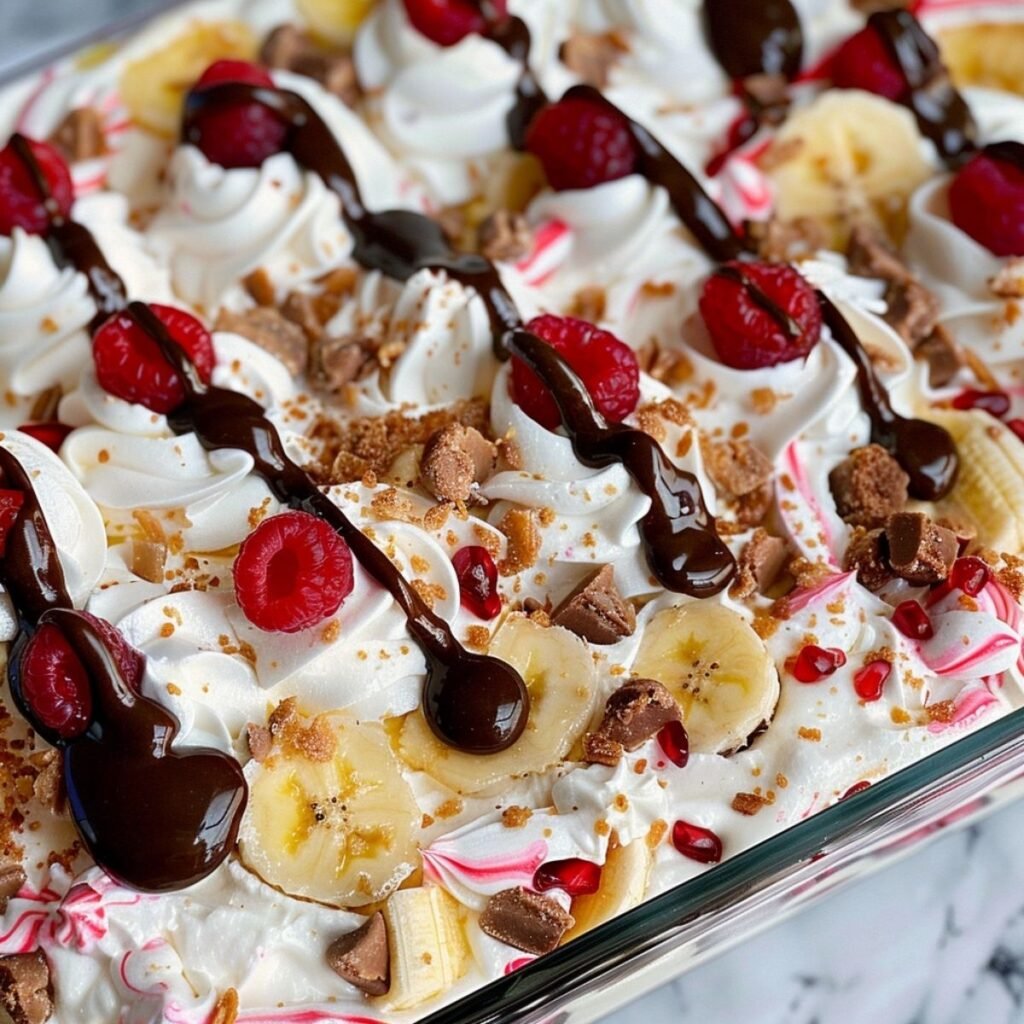Close-up of No-Bake Banana Split Cake showing layered creamy filling, fruit, whipped topping, and chocolate drizzle on a marble surface.