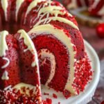 Close-up of Red Velvet Cream Cheese Bundt Cake showing red crumb and creamy swirl, drizzled with glaze on a marble surface.