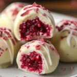 Close-up of White Chocolate Raspberry Cheesecake Balls showing white chocolate shell and raspberry swirl on a marble surface.