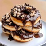 Cookies and Cream Donuts on a ceramic plate, showcasing glossy chocolate ganache dripping down the sides and topped with crushed cookie pieces.