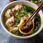 Easy Wonton Soup on a modern marble countertop, showcasing its delicate wontons and golden broth with green onions and chili oil.