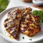 Close-up of juicy grilled chicken showing golden char lines and glistening herb marinade, served on a white ceramic plate with fresh parsley.