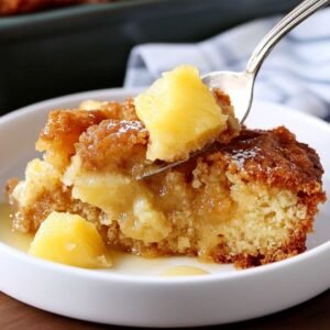 Pineapple Dump Cake on a marble surface, showcasing its golden crisp topping and juicy pineapple chunks on a fork with visible syrup drizzle.
