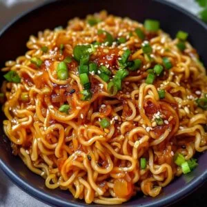 saucy ramen noodles (vegan recipe) on a modern marble countertop, showcasing glossy noodles with sesame seeds and spring onion.