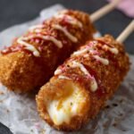 Mozzarella Corn Dog with melted cheese pull and golden crispy crust, topped with ketchup, mayo, and crushed seasoning on parchment paper.