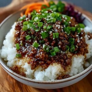 Close-up of Easy Korean Ground Beef Bowl with savory beef in sweet-salty sauce over steamed white rice, topped with fresh green onions and sesame seeds, with carrots and cabbage in the background