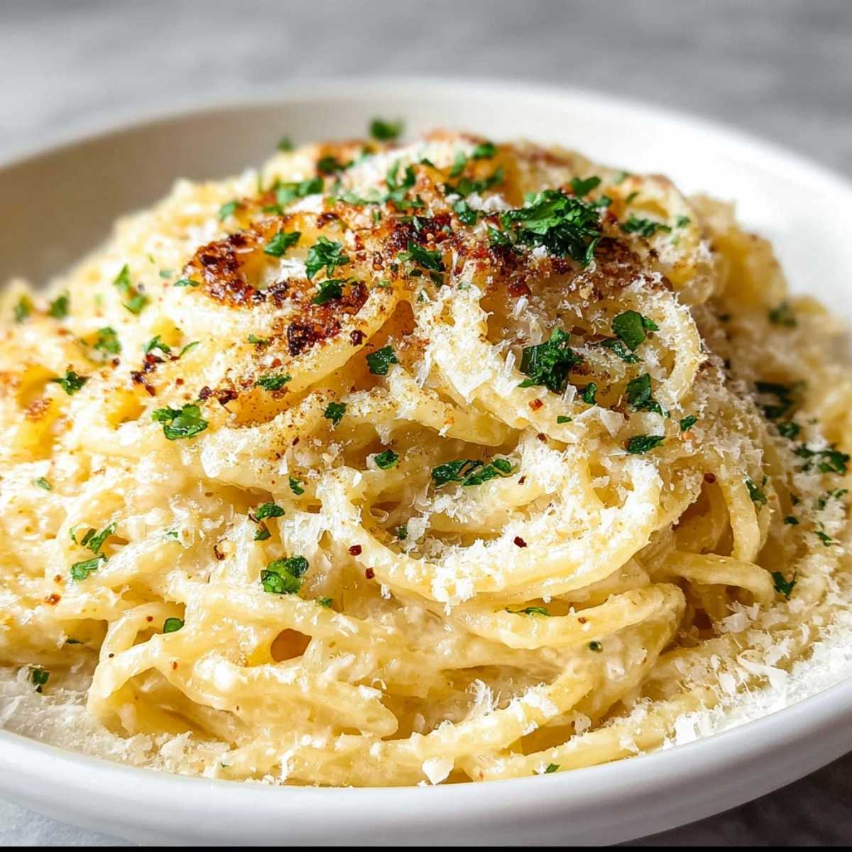 Close-up of Creamy Garlic Pasta showing rich, smooth sauce on spaghetti, topped with grated Parmesan and fresh parsley in a white bowl.