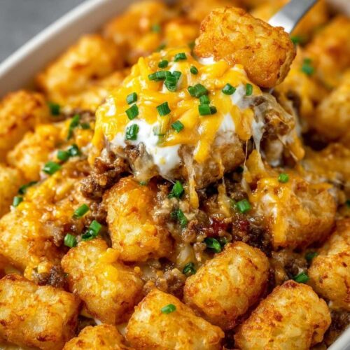 Close-up of Tater Tot Casserole showing the cheesy texture and golden brown tots, garnished with fresh green chives on a spoon.