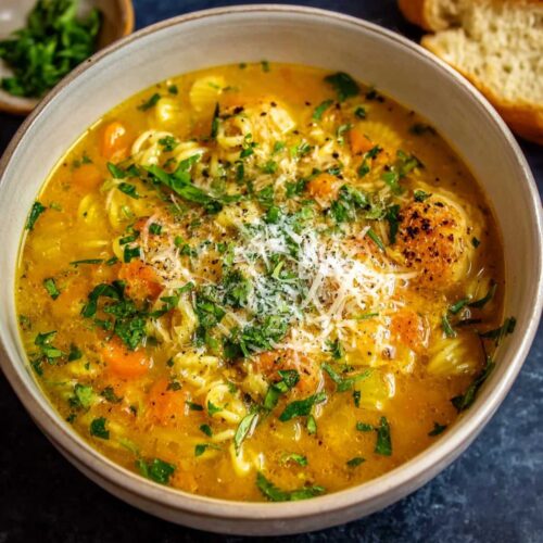 Close-up of Italian Penicillin Soup showing a rich golden broth and small pasta, garnished with fresh parsley and Parmesan cheese in a ceramic bowl