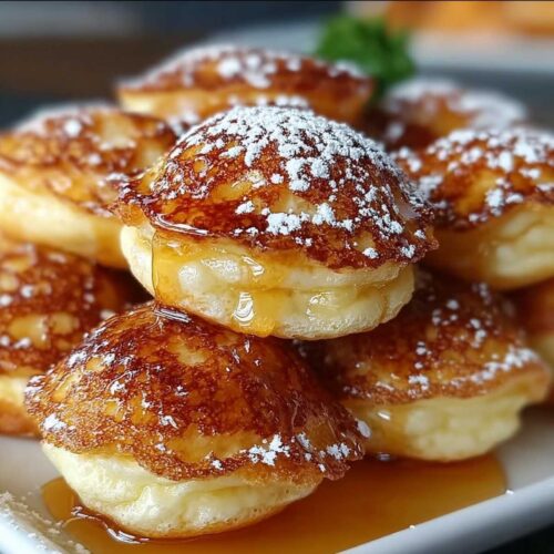 Close-up of fluffy Pancake Poppers on a white plate, showing golden texture, powdered sugar, and dripping maple syrup