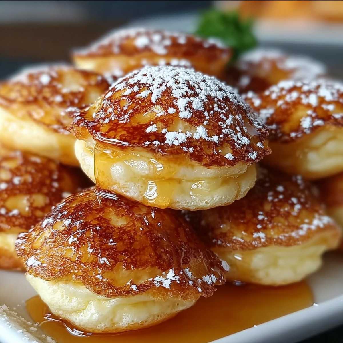 Close-up of fluffy Pancake Poppers on a white plate, showing golden texture, powdered sugar, and dripping maple syrup