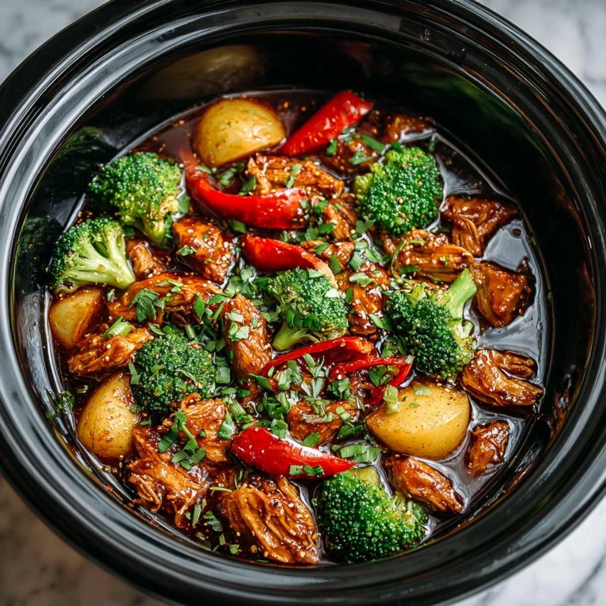 Close-up of Dump and Go Crockpot Teriyaki Chicken showing tender shredded chicken and vibrant broccoli in a glossy teriyaki sauce inside the black slow cooker