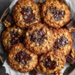 Close-up of dark chocolate chunk molasses oatmeal cookies showing chewy oat texture, melted chocolate centers, and golden baked edges on parchment.