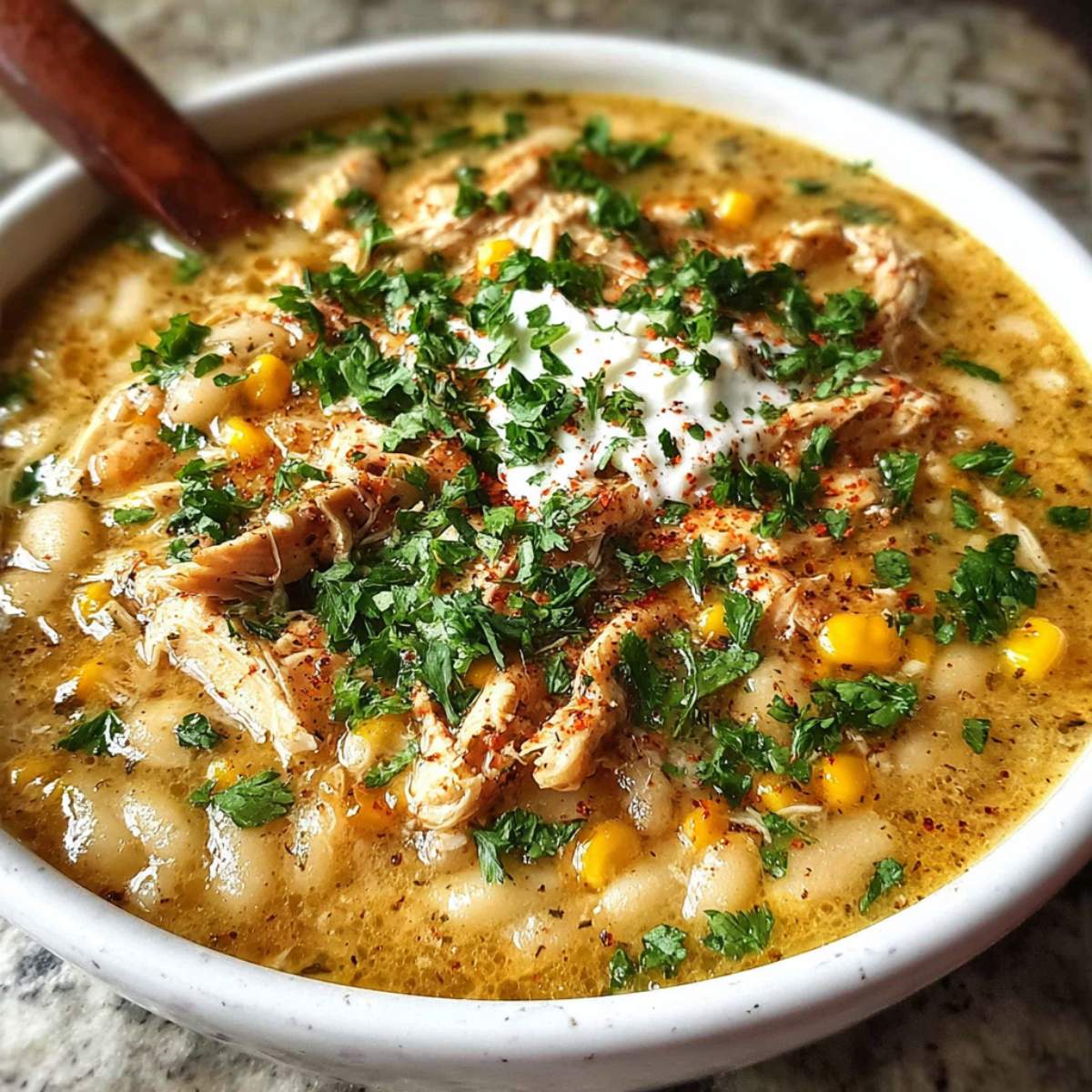 white chicken chili showing creamy broth, shredded chicken, white beans, corn, sour cream, and fresh cilantro.