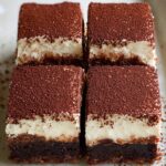 Close-up of tiramisu brownies showing fudgy espresso brownie base, creamy mascarpone layer, and cocoa powder topping on a plate.